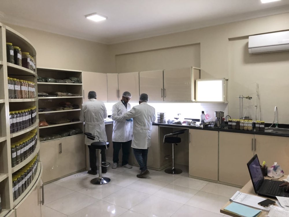 Technicians in lab coats working at the bench of our in-house quality control laboratory, beside shelves of labelled herb samples